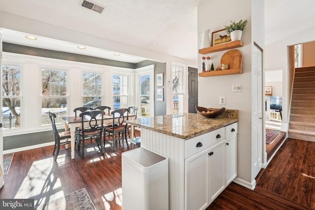 kitchen featuring white cabinets, vaulted ceiling, dark stone counters, and dark wood-type flooring