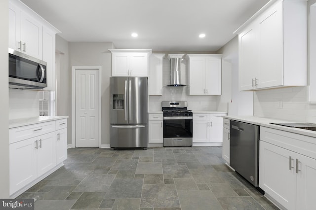 kitchen featuring white cabinets, decorative backsplash, stainless steel appliances, and wall chimney range hood