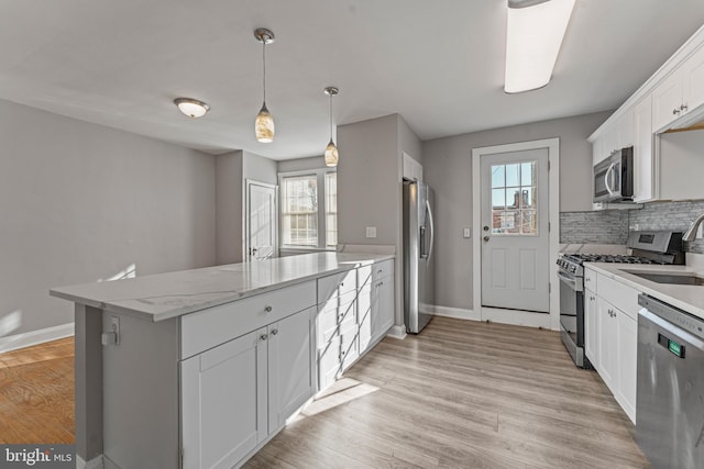 kitchen featuring kitchen peninsula, decorative backsplash, appliances with stainless steel finishes, decorative light fixtures, and white cabinetry