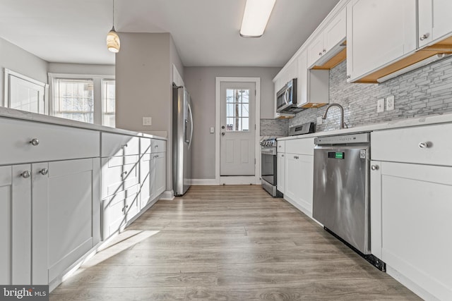 kitchen featuring a healthy amount of sunlight, white cabinets, hanging light fixtures, and appliances with stainless steel finishes