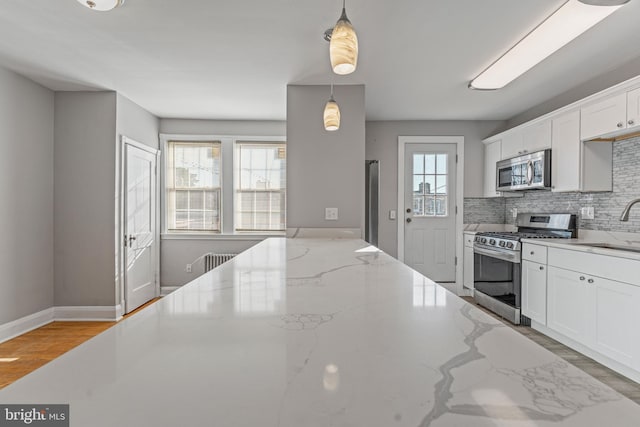 kitchen featuring stainless steel appliances, light stone counters, backsplash, plenty of natural light, and decorative light fixtures