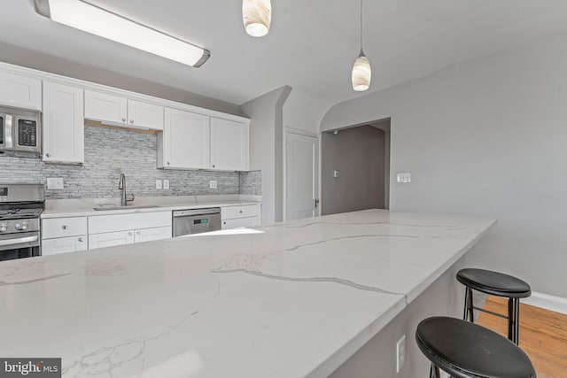 kitchen with decorative backsplash, stainless steel appliances, sink, white cabinetry, and hanging light fixtures