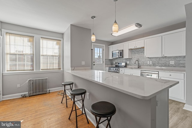 kitchen with radiator, hanging light fixtures, appliances with stainless steel finishes, a kitchen bar, and white cabinetry