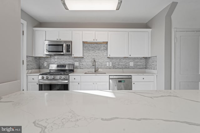 kitchen with decorative backsplash, light stone counters, stainless steel appliances, sink, and white cabinetry