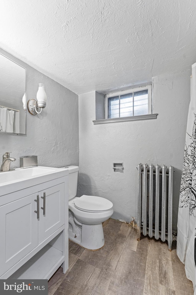 bathroom featuring radiator heating unit, a textured ceiling, toilet, vanity, and hardwood / wood-style flooring