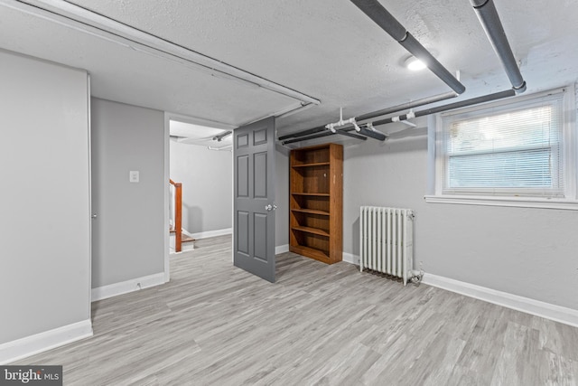 basement with a textured ceiling, light hardwood / wood-style floors, and radiator