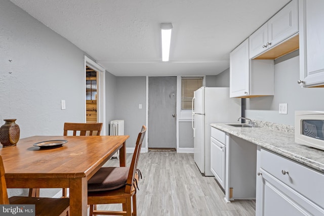 kitchen featuring sink, radiator heating unit, a textured ceiling, white appliances, and white cabinets