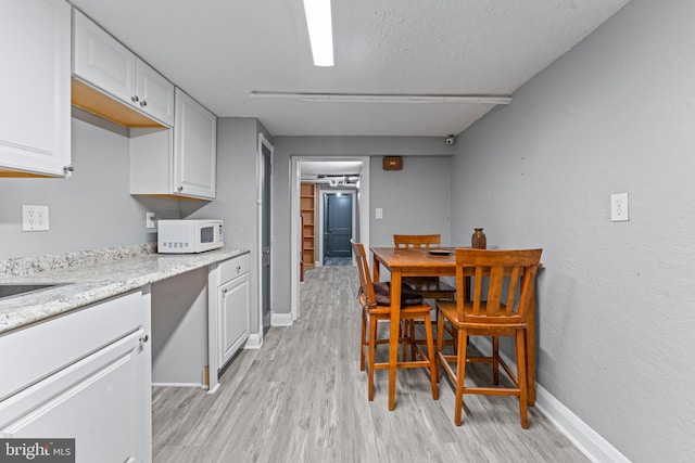 kitchen featuring light stone counters, light hardwood / wood-style flooring, white cabinets, and a textured ceiling