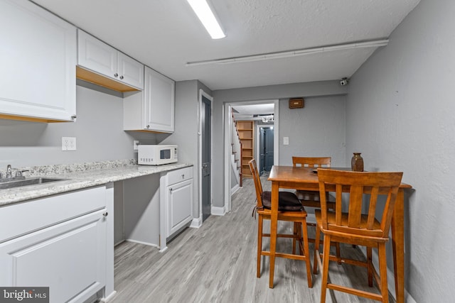 kitchen featuring white cabinets, a textured ceiling, light hardwood / wood-style flooring, and sink