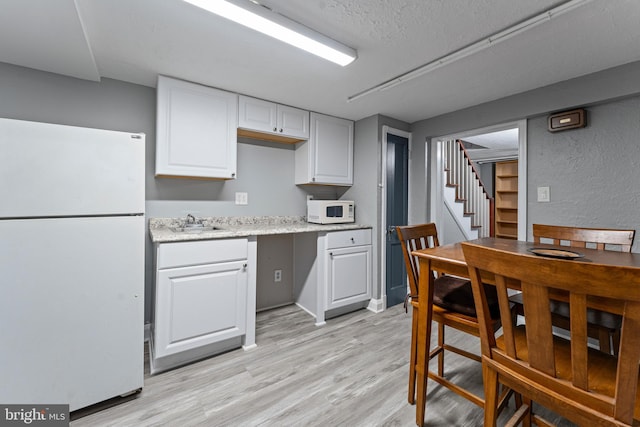 kitchen with a textured ceiling, white appliances, sink, light hardwood / wood-style flooring, and white cabinetry