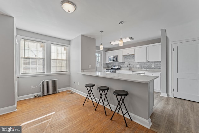 kitchen featuring kitchen peninsula, appliances with stainless steel finishes, a breakfast bar, radiator heating unit, and white cabinetry