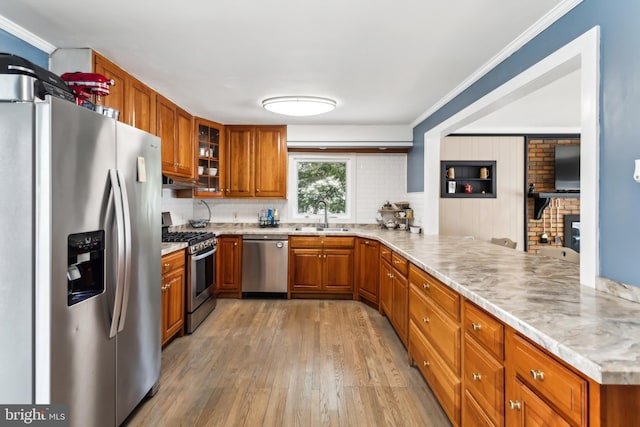 kitchen featuring appliances with stainless steel finishes, sink, kitchen peninsula, crown molding, and light wood-type flooring