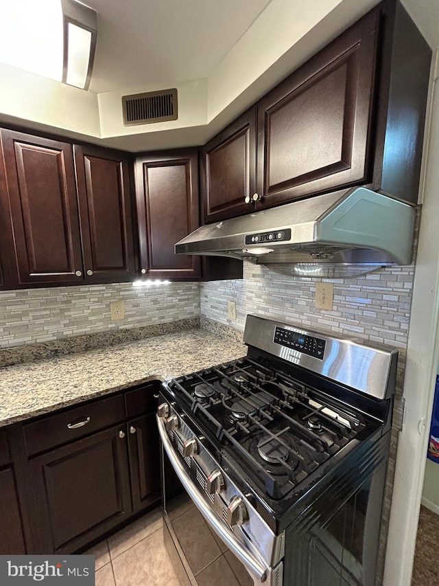 kitchen featuring light stone countertops, backsplash, dark brown cabinets, light tile patterned floors, and stainless steel range with gas stovetop