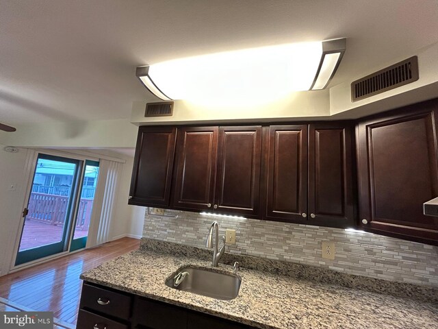 kitchen featuring sink, light stone countertops, tasteful backsplash, light hardwood / wood-style floors, and dark brown cabinetry