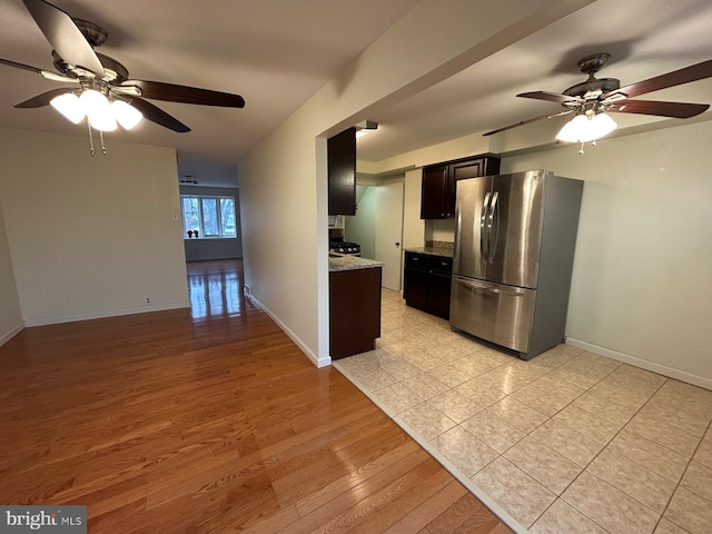 kitchen with stainless steel refrigerator, ceiling fan, light stone counters, black gas stove, and light wood-type flooring