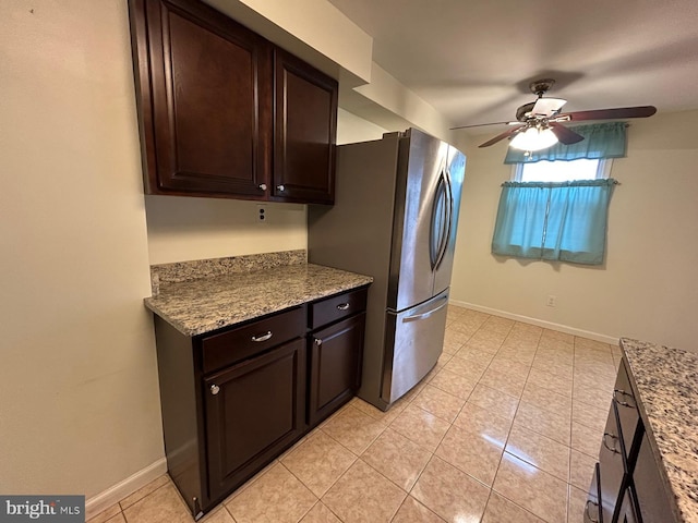 kitchen featuring stainless steel refrigerator, light stone countertops, dark brown cabinetry, ceiling fan, and light tile patterned floors