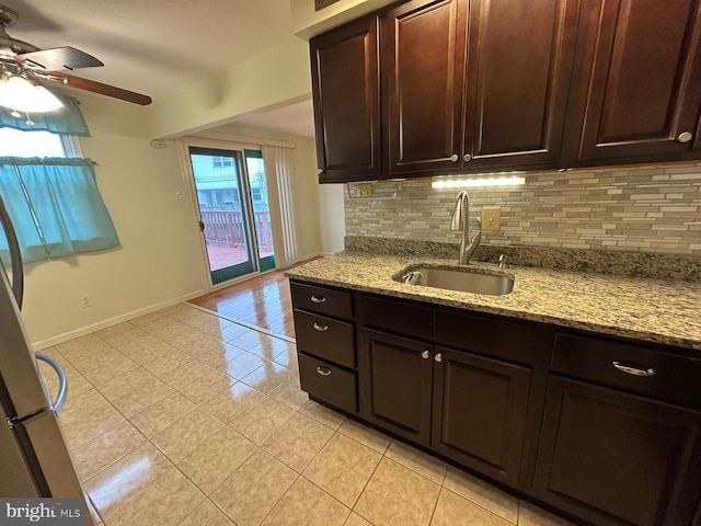 kitchen with light stone countertops, backsplash, dark brown cabinetry, sink, and light tile patterned floors