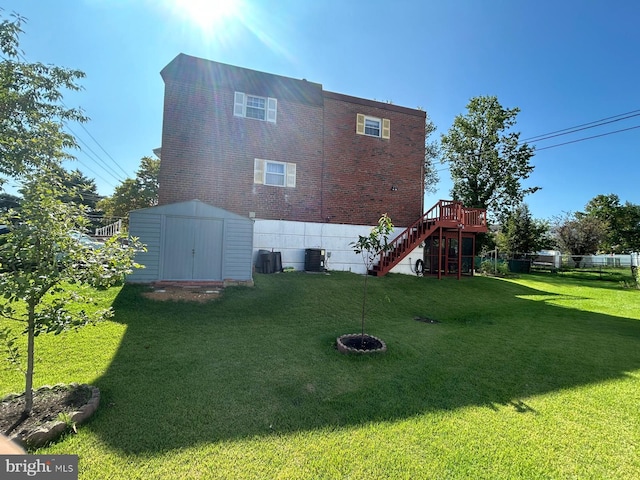 rear view of property with a lawn, cooling unit, and a storage shed