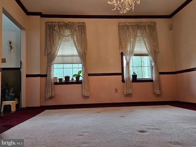 empty room featuring a notable chandelier, crown molding, and carpet floors