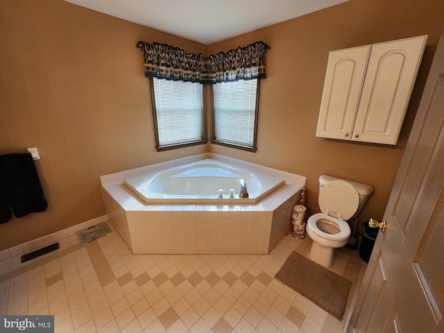 bathroom with a relaxing tiled tub, toilet, and tile patterned flooring