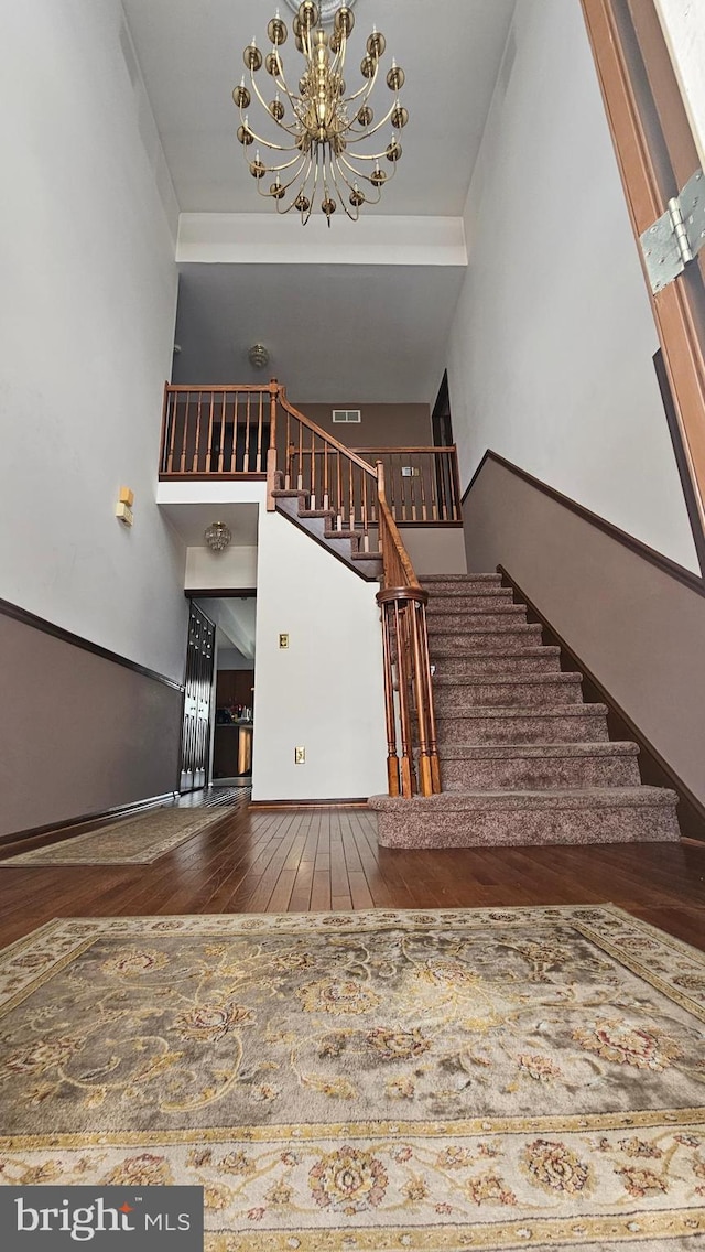 staircase featuring a high ceiling, a notable chandelier, and hardwood / wood-style flooring