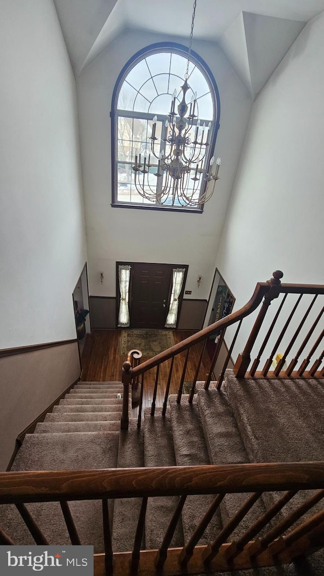 staircase featuring hardwood / wood-style flooring, high vaulted ceiling, and a chandelier