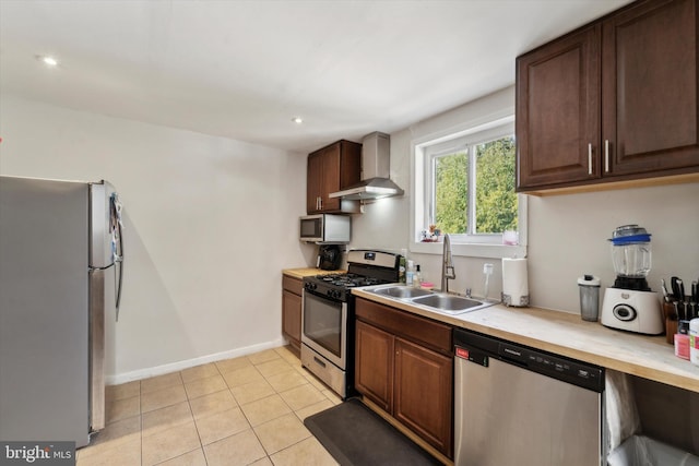 kitchen featuring wall chimney range hood, sink, light tile patterned floors, appliances with stainless steel finishes, and dark brown cabinets