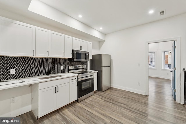 kitchen featuring white cabinets, sink, decorative backsplash, light wood-type flooring, and appliances with stainless steel finishes