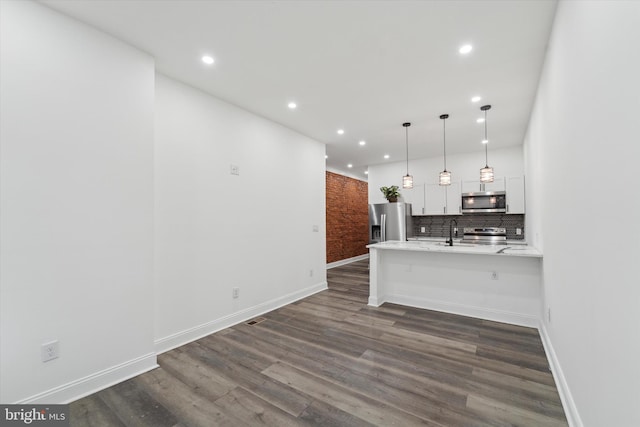 kitchen with hanging light fixtures, appliances with stainless steel finishes, white cabinetry, a breakfast bar area, and brick wall