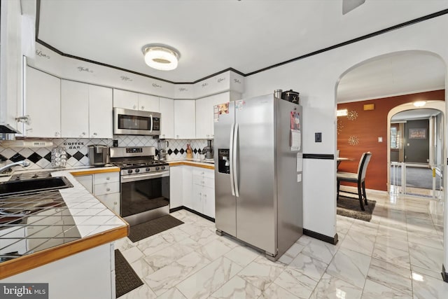 kitchen featuring tile countertops, white cabinets, sink, tasteful backsplash, and stainless steel appliances