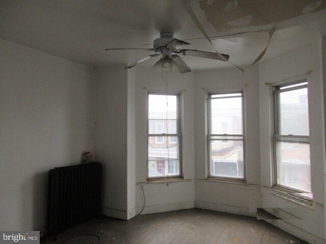 unfurnished room featuring light hardwood / wood-style floors, ceiling fan, a healthy amount of sunlight, and radiator heating unit