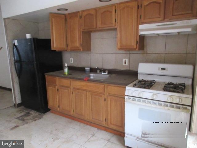 kitchen with tasteful backsplash, black fridge, gas range gas stove, and sink