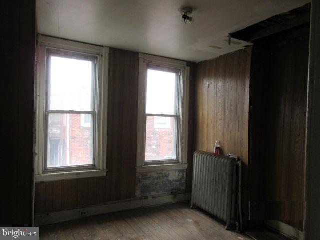 unfurnished room featuring radiator, wood walls, and a wealth of natural light