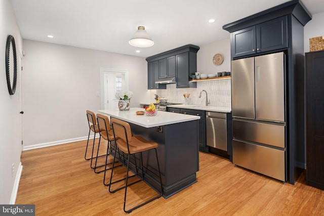 kitchen featuring a center island, a kitchen breakfast bar, light hardwood / wood-style flooring, decorative backsplash, and appliances with stainless steel finishes