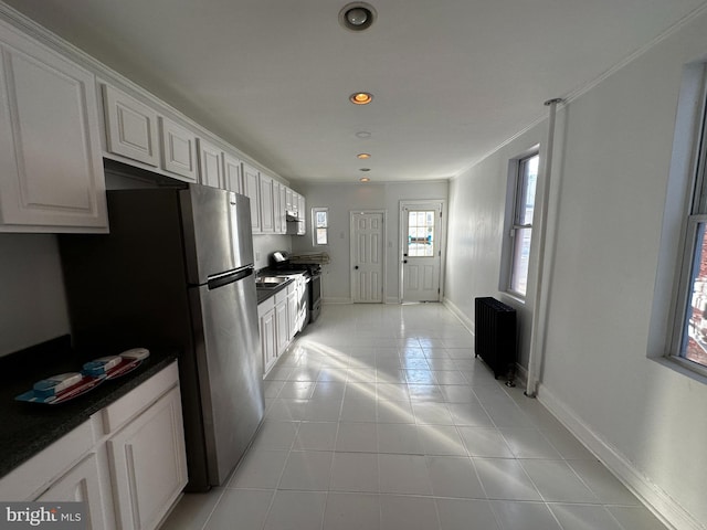 kitchen with stainless steel appliances, white cabinetry, radiator, and light tile patterned flooring