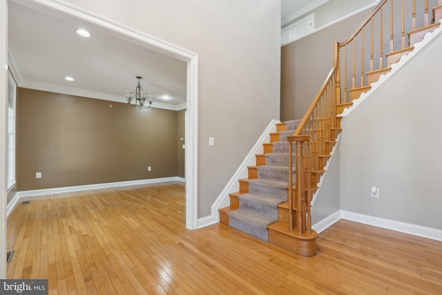 stairs with hardwood / wood-style floors, ornamental molding, and a chandelier