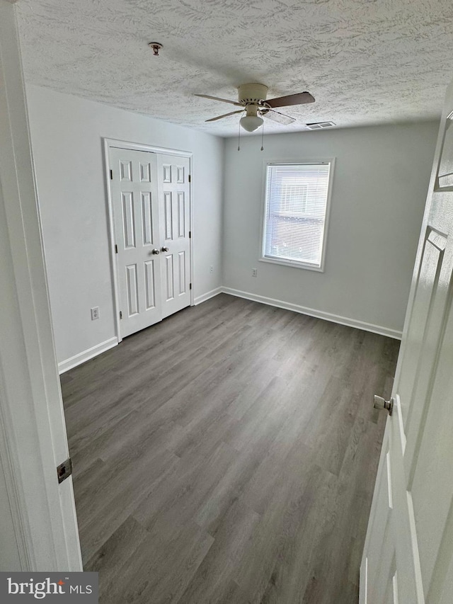 unfurnished bedroom featuring a textured ceiling, dark wood-type flooring, and ceiling fan