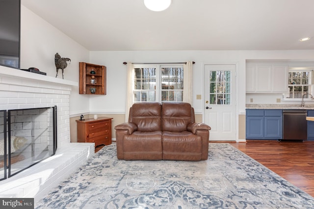 living room featuring a brick fireplace, a healthy amount of sunlight, sink, and dark hardwood / wood-style flooring