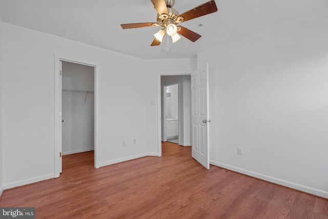 unfurnished bedroom with a spacious closet, a closet, ceiling fan, and light wood-type flooring