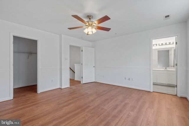 unfurnished bedroom featuring ensuite bathroom, a spacious closet, light hardwood / wood-style flooring, a closet, and ceiling fan