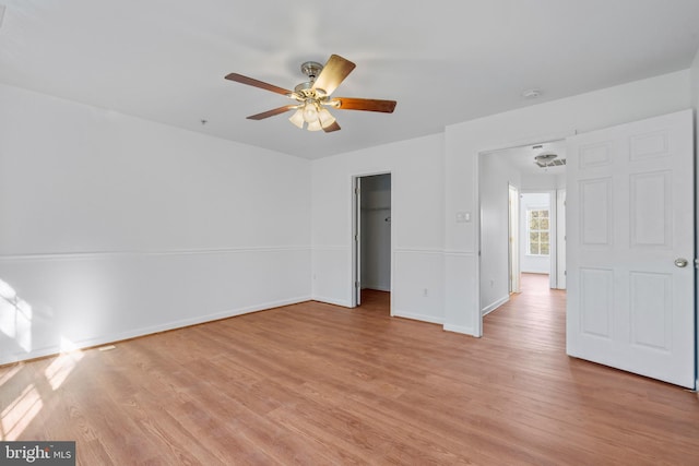 unfurnished bedroom featuring ceiling fan, a spacious closet, a closet, and light wood-type flooring