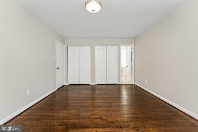 unfurnished bedroom featuring dark hardwood / wood-style flooring and two closets