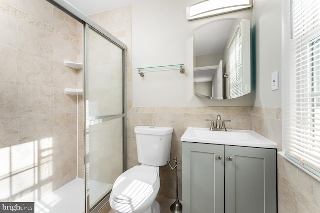 bathroom with vanity, a shower with shower door, tile walls, and toilet