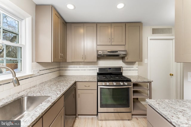 kitchen featuring sink, decorative backsplash, a wealth of natural light, appliances with stainless steel finishes, and light stone counters