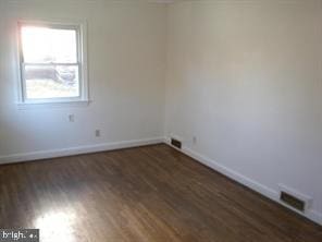 spare room with dark wood-style floors, visible vents, and baseboards