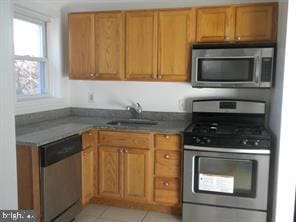 kitchen featuring light tile patterned floors, stainless steel appliances, brown cabinetry, and a sink