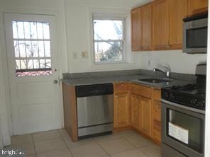 kitchen with light tile patterned floors, dark countertops, brown cabinets, stainless steel appliances, and a sink