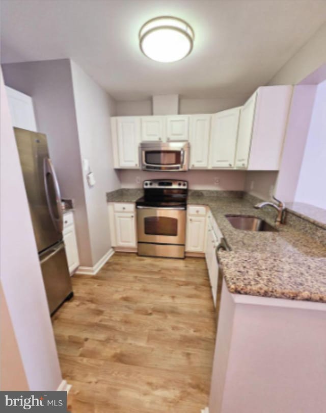 kitchen featuring sink, light stone countertops, light wood-type flooring, white cabinetry, and stainless steel appliances