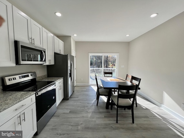 kitchen with light stone counters, white cabinetry, light wood-type flooring, and appliances with stainless steel finishes