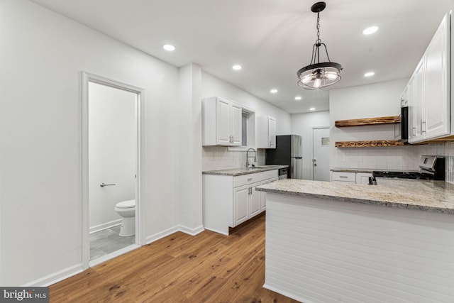 kitchen featuring kitchen peninsula, stainless steel appliances, pendant lighting, light hardwood / wood-style flooring, and white cabinetry